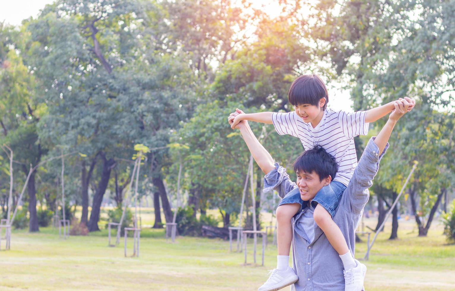 Father and cute son playing paper plane in the park. The son is on the back of his father photo