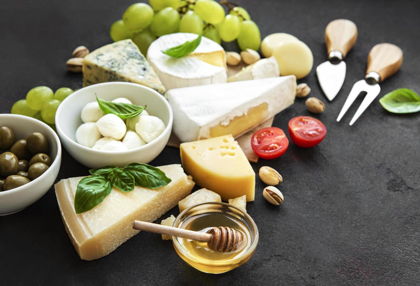 Various types of cheese, grapes, honey, and snacks on a black concrete background photo