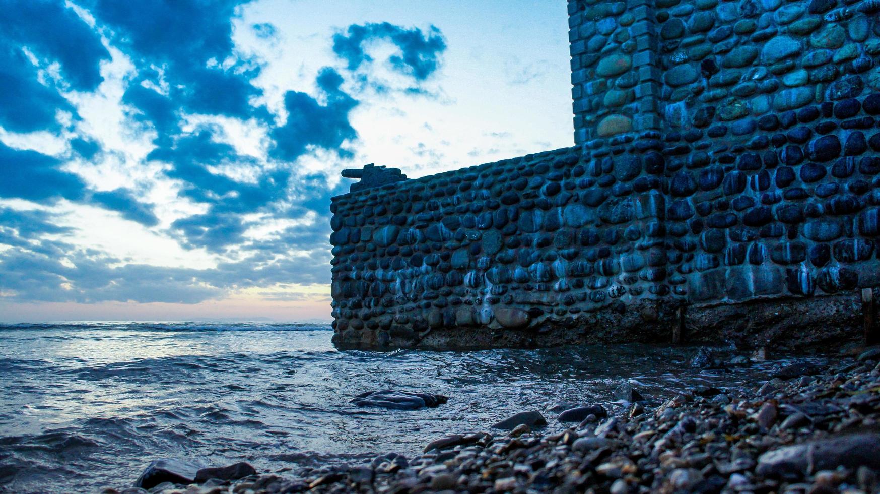 Stone wall with a gun on the background of the sea landscape. photo