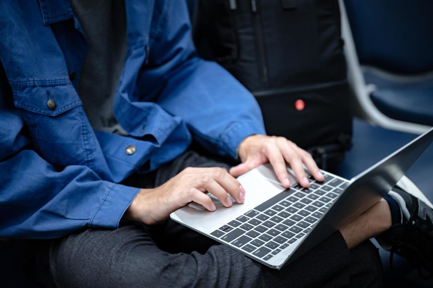 Businessman sitting and using a laptop computer to work at the airport, young person traveling, journey and having internet communication technology for work when waiting indoors at an airport for departure photo