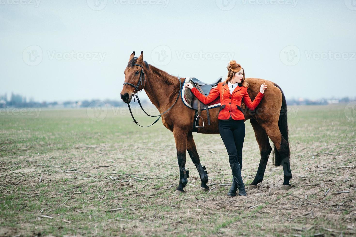 jockey pelirroja con un cárdigan rojo y botas altas negras con un caballo foto