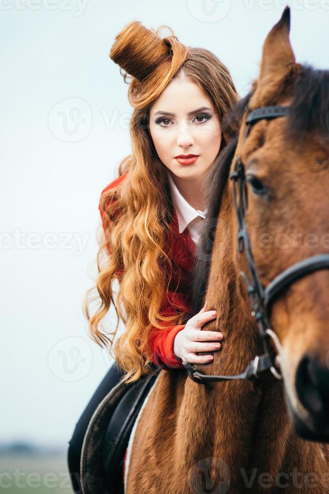 jockey pelirroja con un cárdigan rojo y botas altas negras con un caballo foto