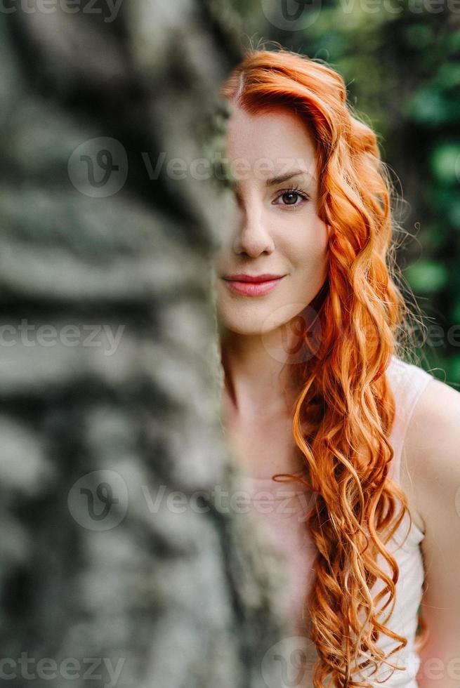 Red-haired young girl walking in a park between trees and architectural objects photo