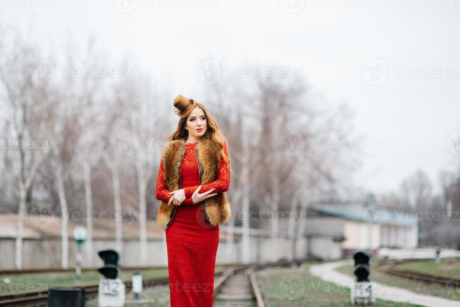 Young girl with red hair in a bright red dress on the railway tracks photo
