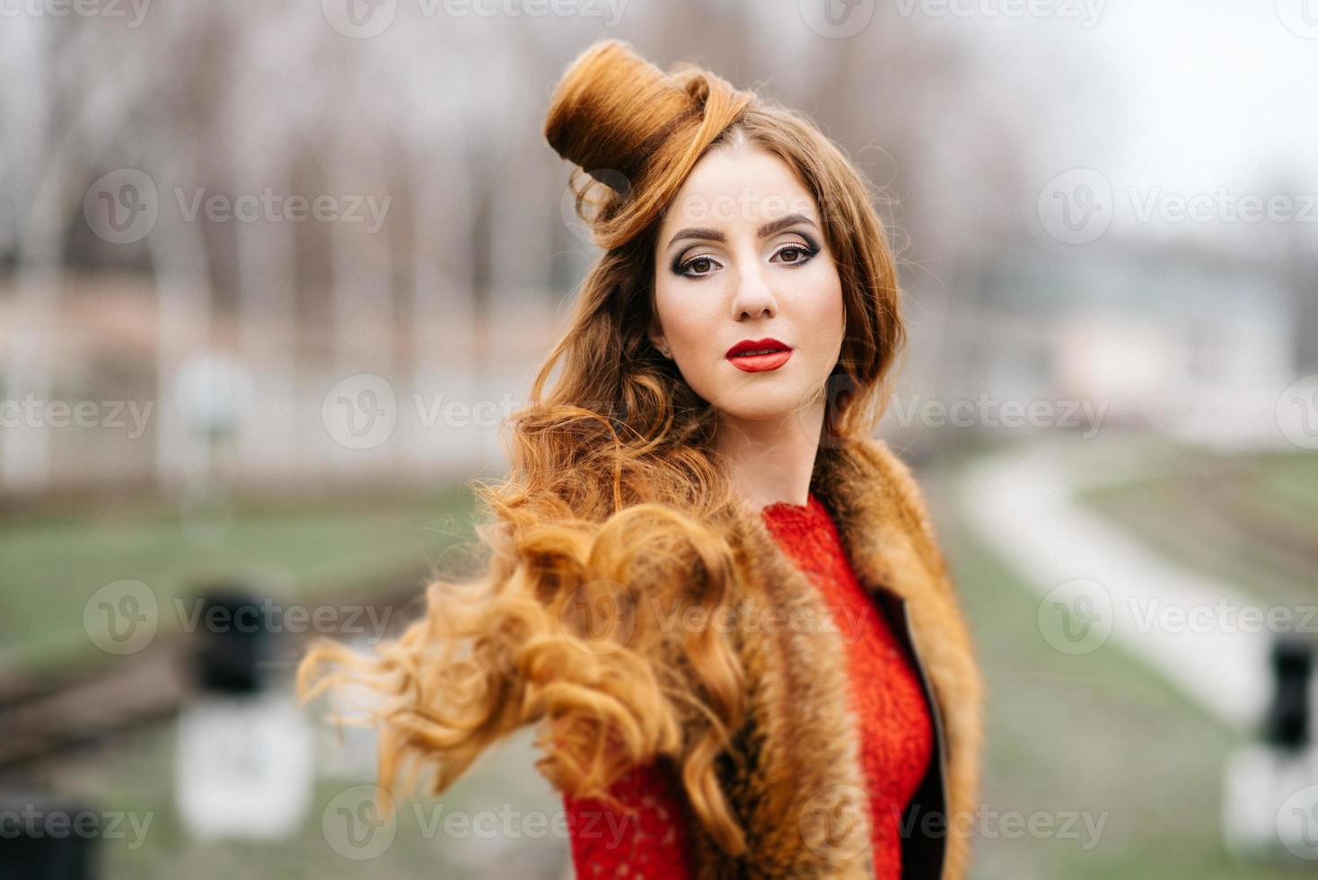 Young girl with red hair in a bright red dress on the railway tracks photo