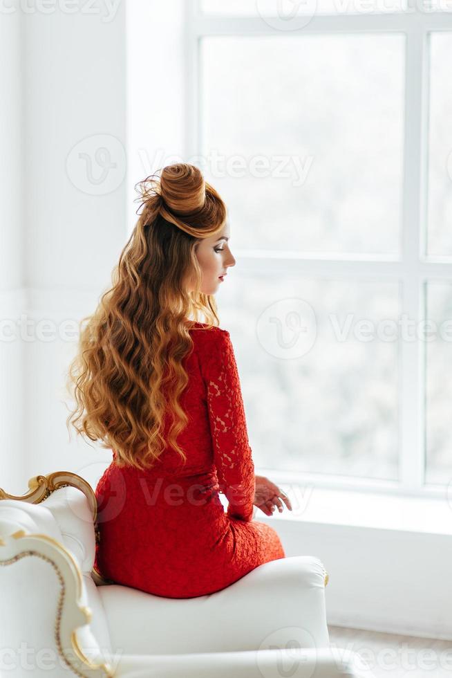 Young girl with red hair in a bright red dress in a bright room photo