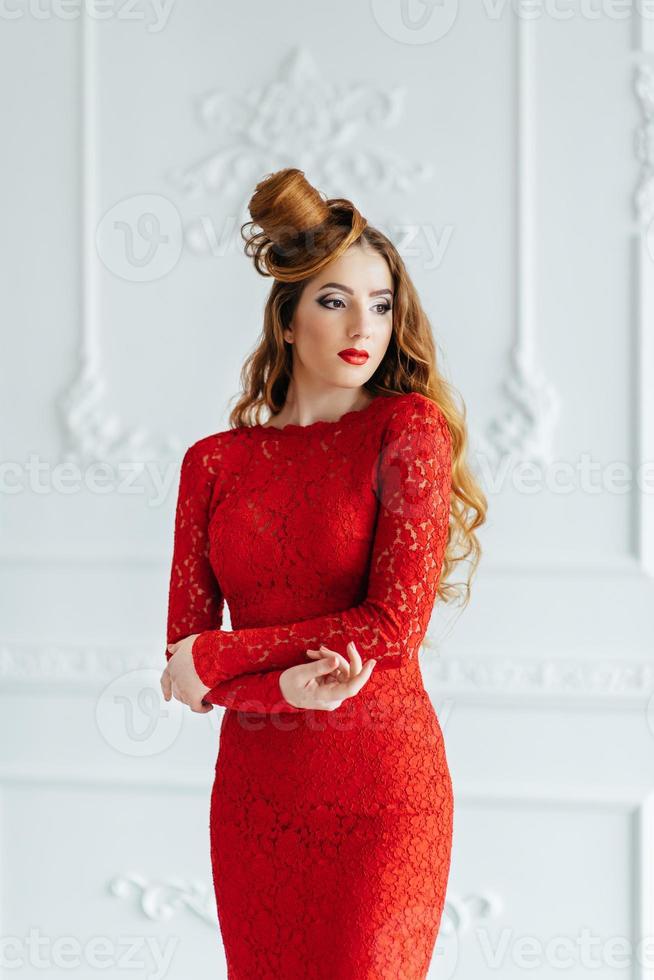 Chica joven con el pelo rojo con un vestido rojo brillante en una habitación luminosa foto