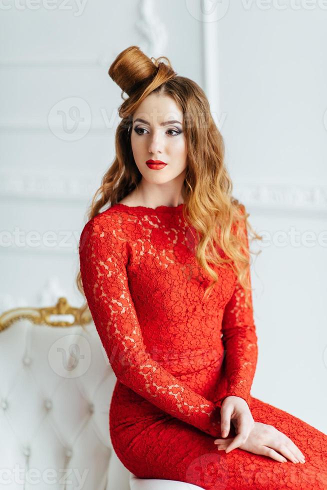 Young girl with red hair in a bright red dress in a bright room photo