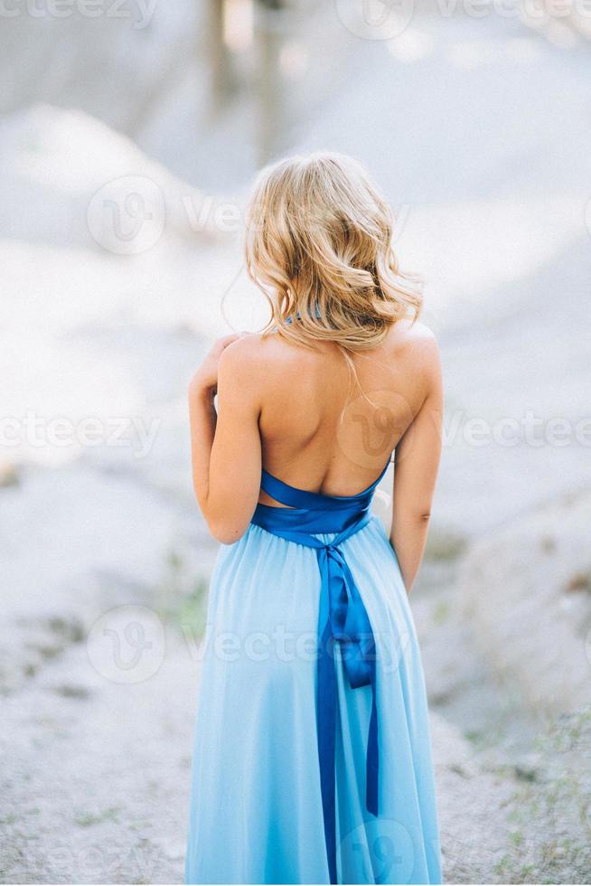 Chica rubia con un vestido azul claro en una cantera de granito foto