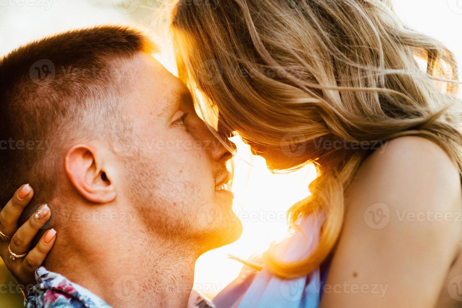 Blonde girl with loose hair in a light blue dress and a guy in the light of sunset photo