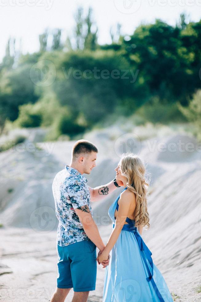 chica rubia con un vestido azul claro y un chico con una camisa ligera en una cantera de granito foto