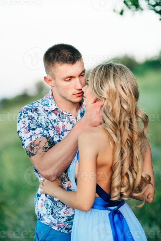 chica rubia con el pelo suelto con un vestido azul claro y un chico a la luz del atardecer foto