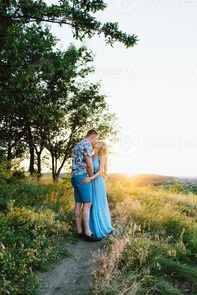 chica rubia con el pelo suelto con un vestido azul claro y un chico a la luz del atardecer foto