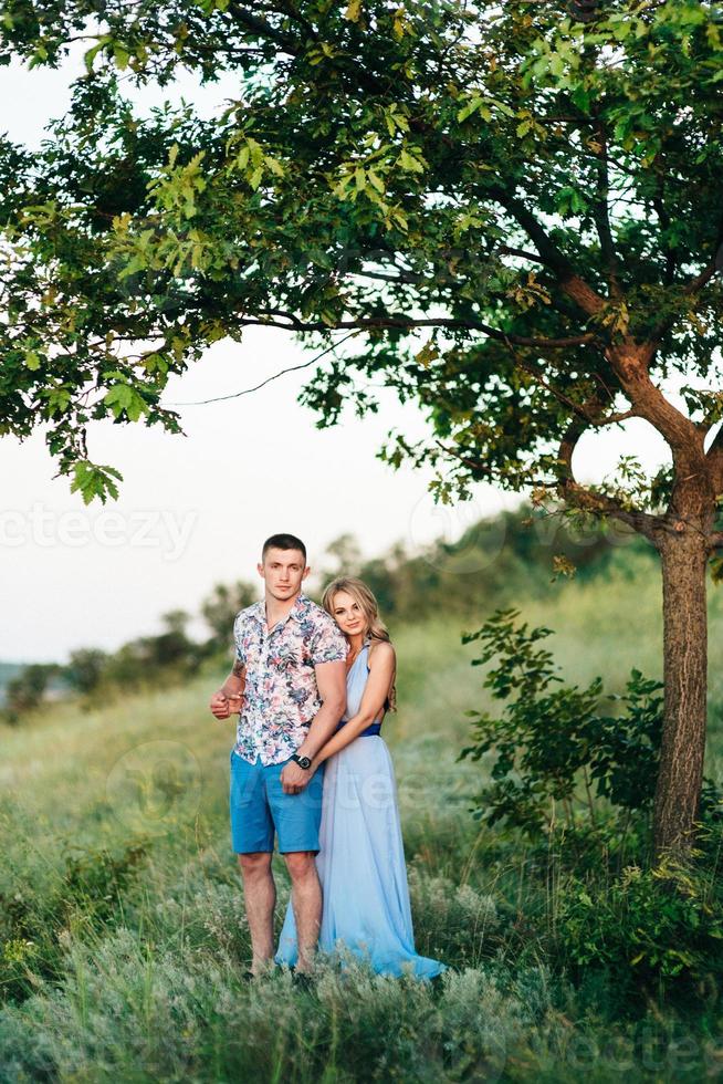 Blonde girl with loose hair in a light blue dress and a guy in the light of sunset photo