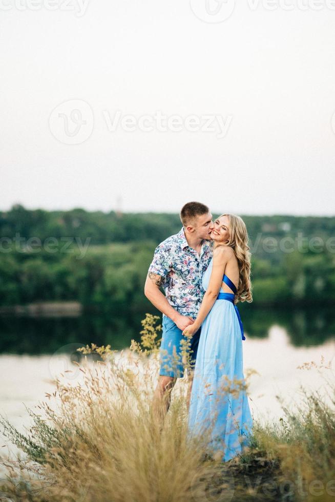 Blonde girl with loose hair in a light blue dress and a guy in the light of sunset photo