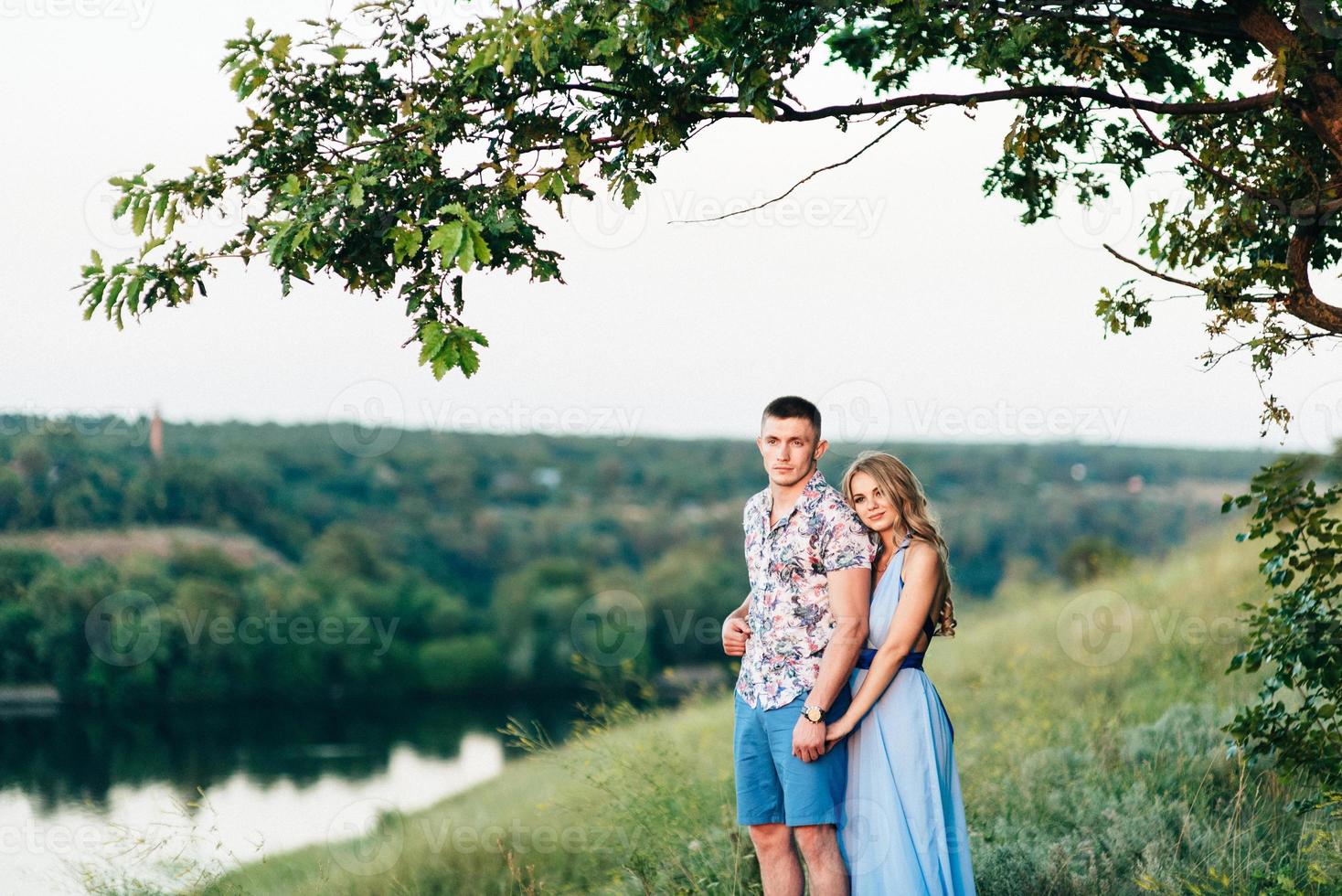 Blonde girl with loose hair in a light blue dress and a guy in the light of sunset photo