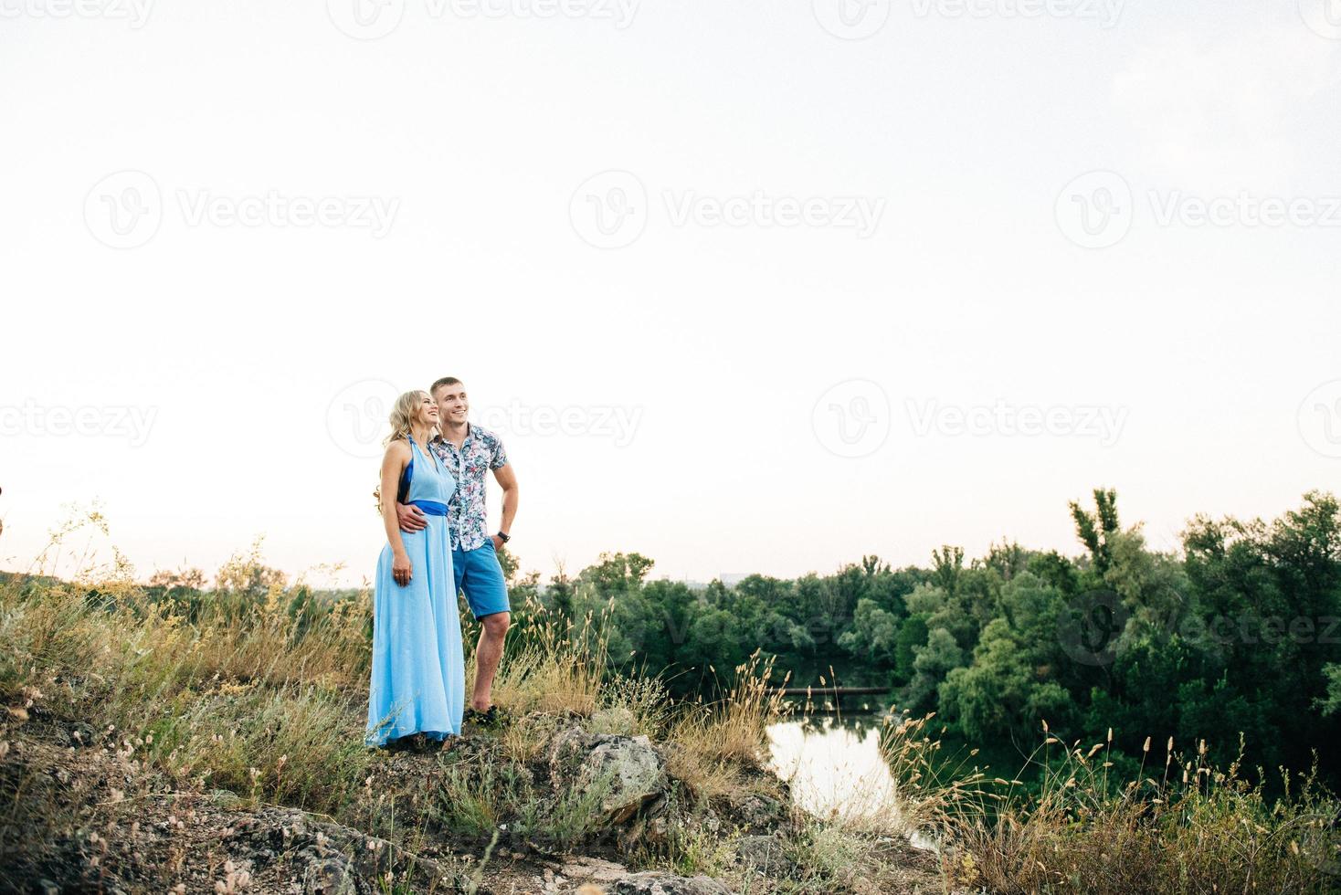 Blonde girl with loose hair in a light blue dress and a guy in the light of sunset photo