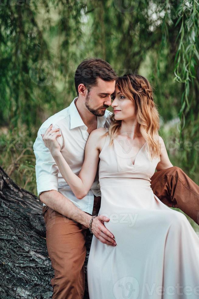 A guy and a girl are sitting together on a crooked tree on the steep bank photo