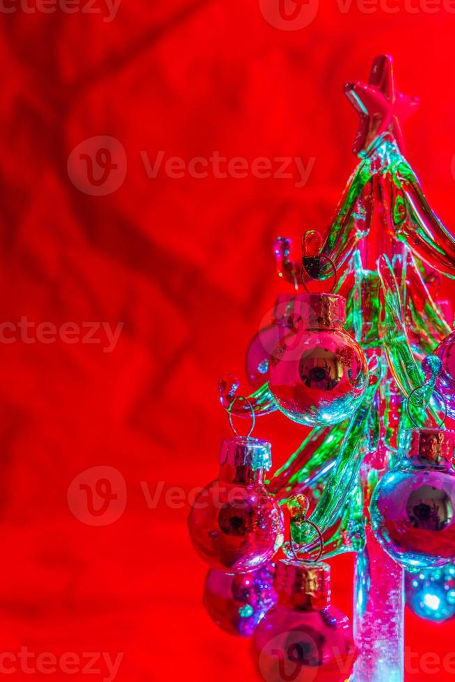 Mini árbol de Navidad de vidrio iluminado y contra un fondo rojo. foto