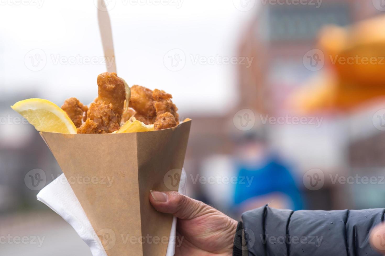 Mano masculina sosteniendo pescado y patatas fritas británicas en un cono de papel foto