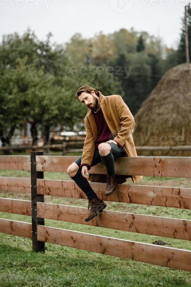 man in a brown coat on a wooden fence photo