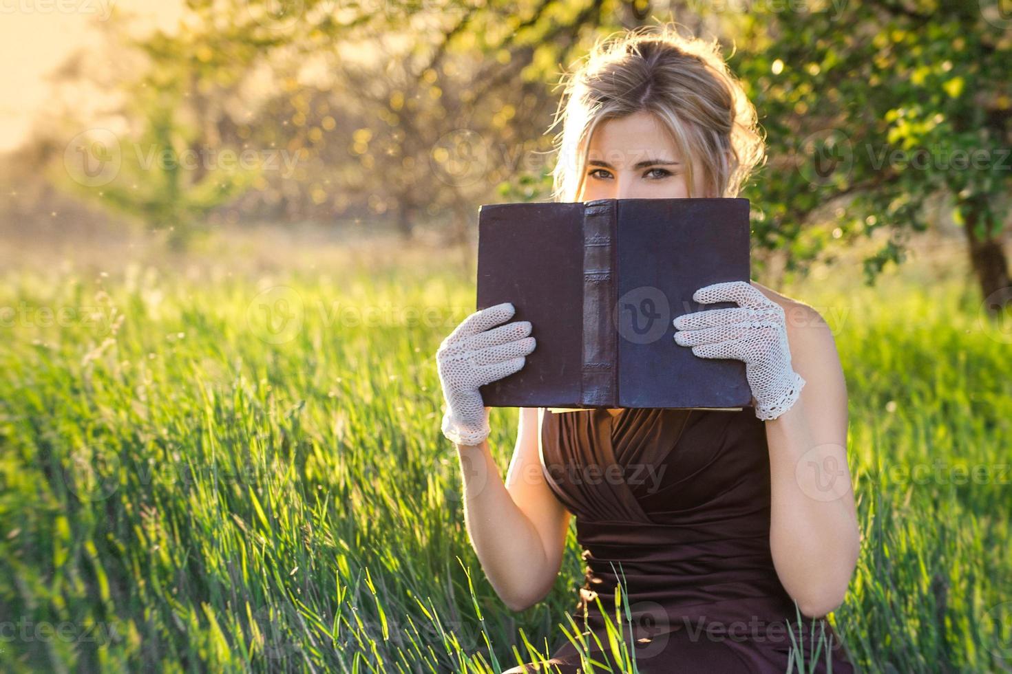 young blonde girl in a brown vintage dress and top hat reads a book photo