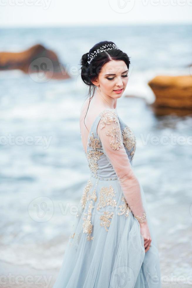 bride in a blue light dress walking along the ocean photo