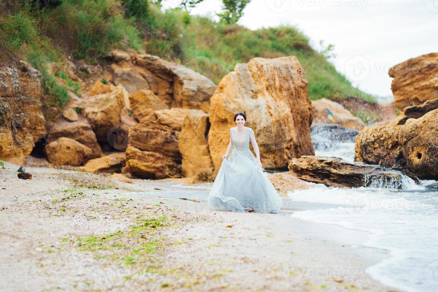 bride in a blue light dress walking along the ocean photo