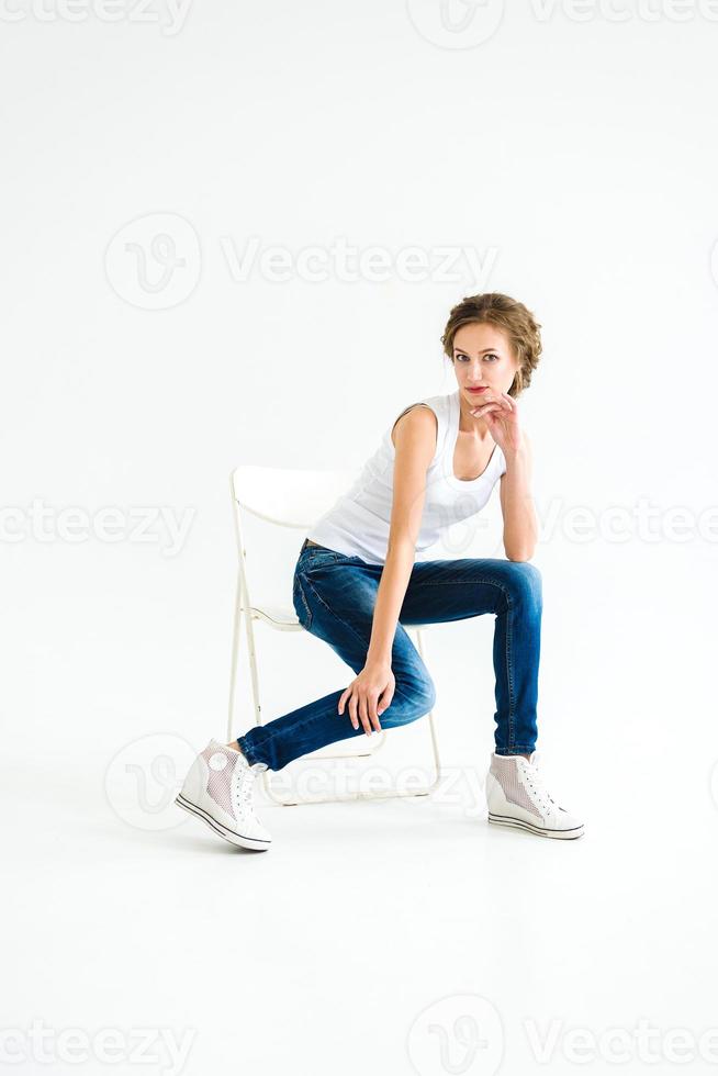 Chica alegre en una camiseta blanca y jeans azul oscuro en el estudio sobre un fondo blanco. foto