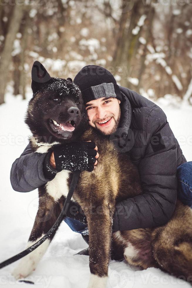 A man in a jacket and a knitted hat walks with an American Akita dog photo