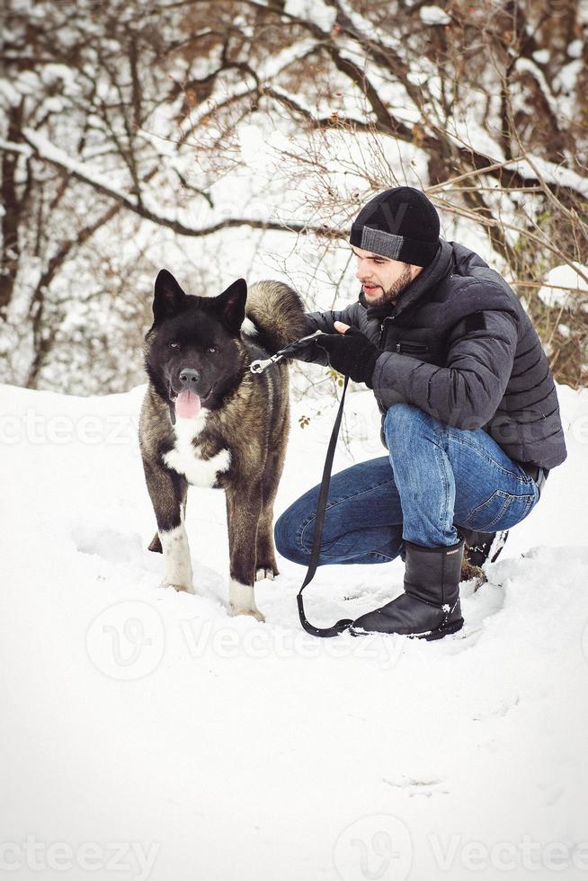 A man in a jacket and a knitted hat walks with an American Akita dog photo