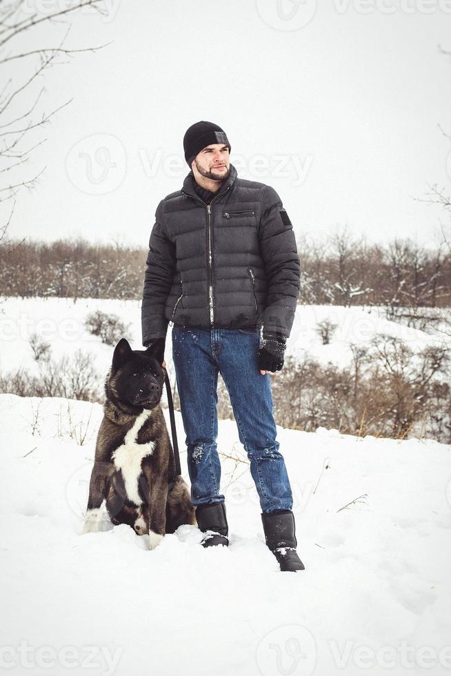 A man in a jacket and a knitted hat walks with an American Akita dog photo