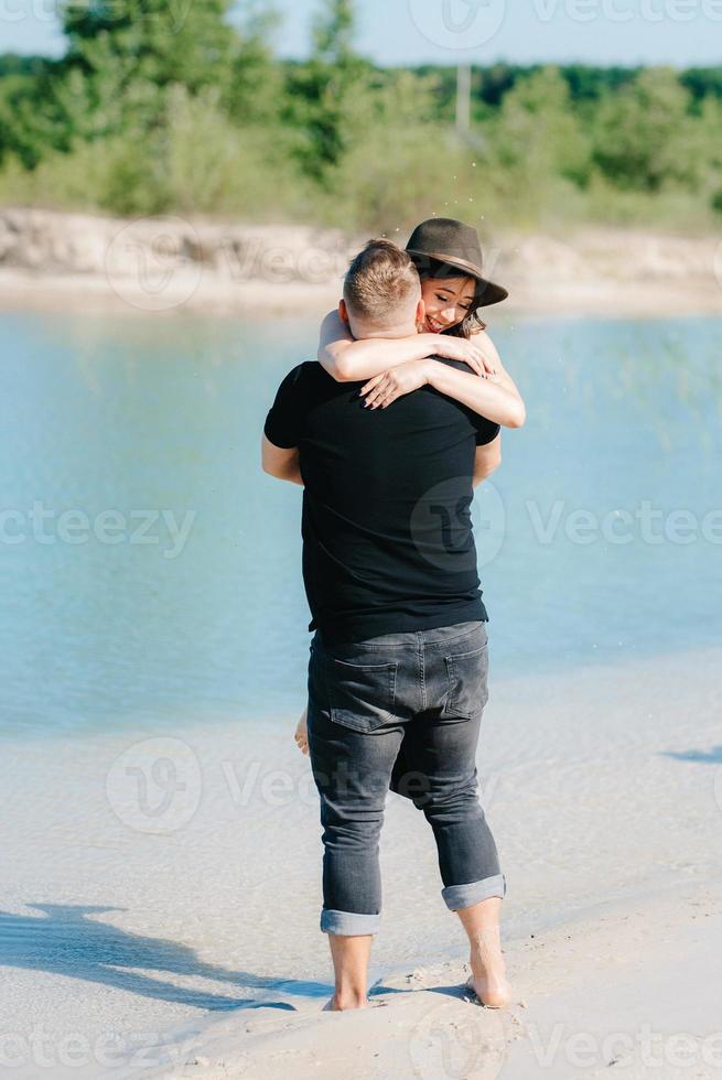 Pareja joven un chico con una chica vestida de negro están caminando sobre la arena blanca foto