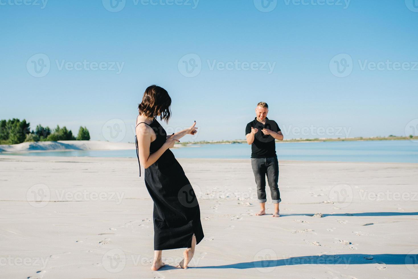 young couple a guy with a girl in black clothes are walking on the white sand photo