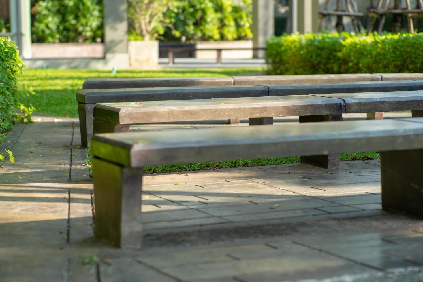 Selective focus of empty concrete benches in an outdoor park with blurred green bush in the background photo