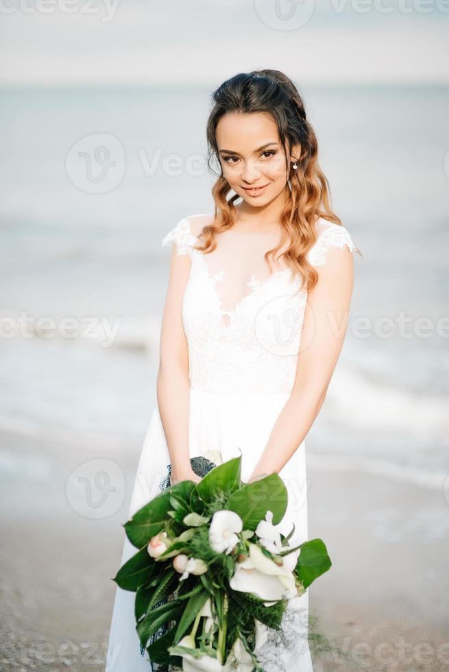 novia con un ramo de novia en la orilla del mar foto