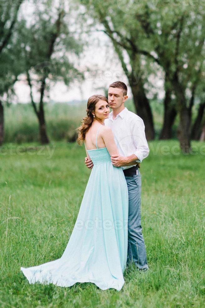 happy guy in a white shirt and a girl in a turquoise dress are walking in the forest park photo