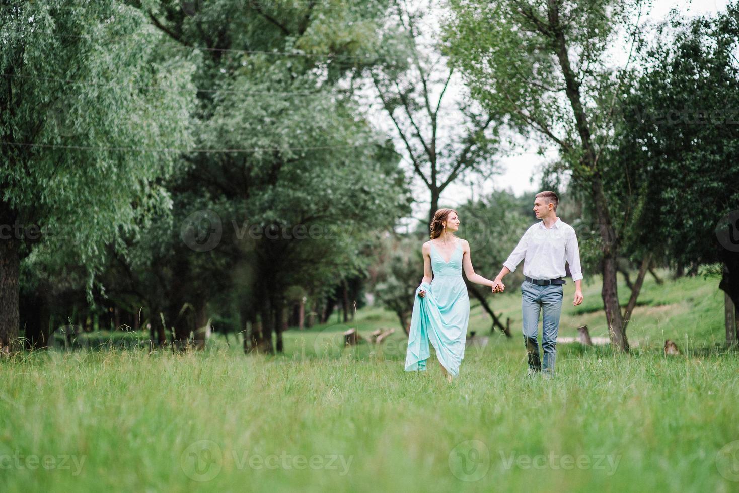 happy guy in a white shirt and a girl in a turquoise dress are walking in the forest park photo