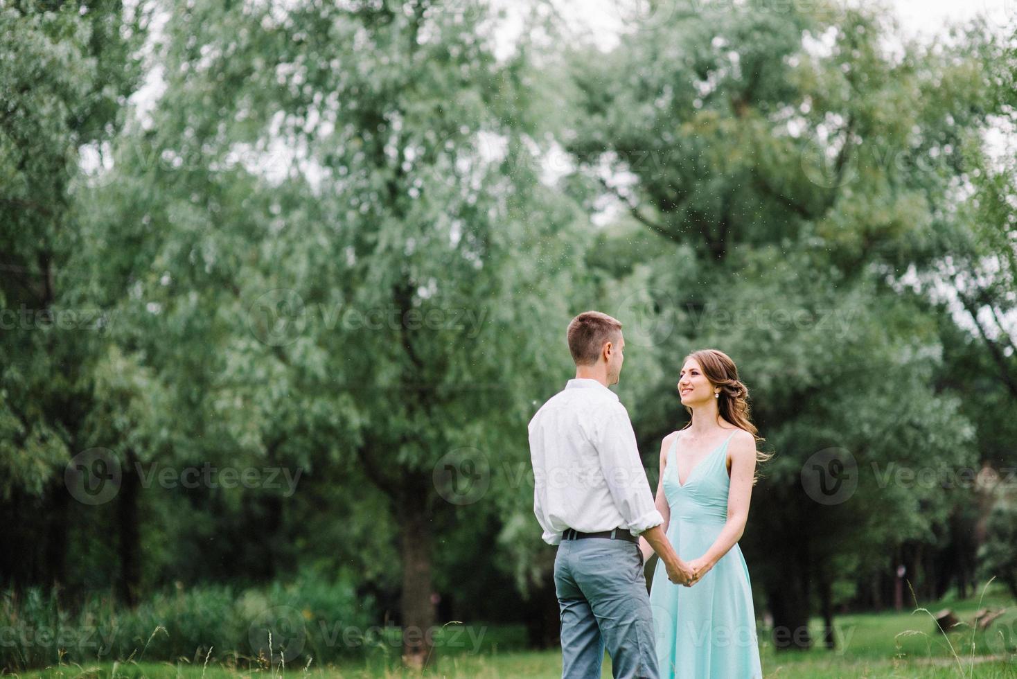 chico feliz con una camisa blanca y una chica con un vestido turquesa están caminando en el parque forestal foto