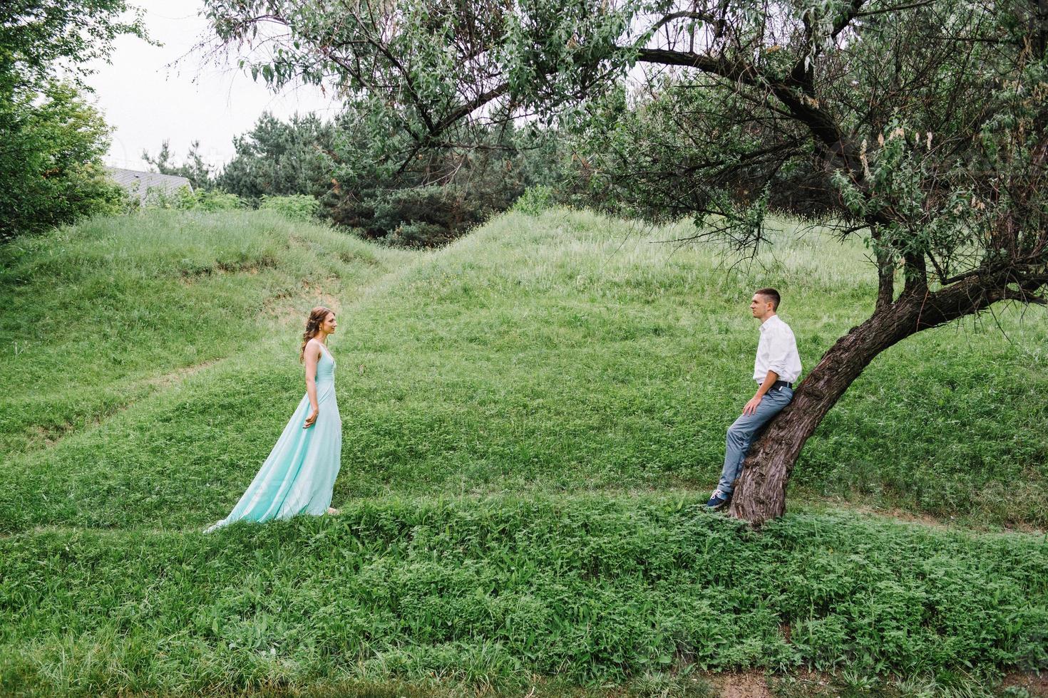 happy guy in a white shirt and a girl in a turquoise dress are walking in the forest park photo