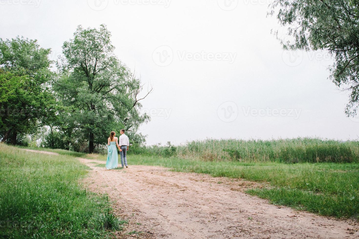 chico feliz con una camisa blanca y una chica con un vestido turquesa están caminando en el parque forestal foto