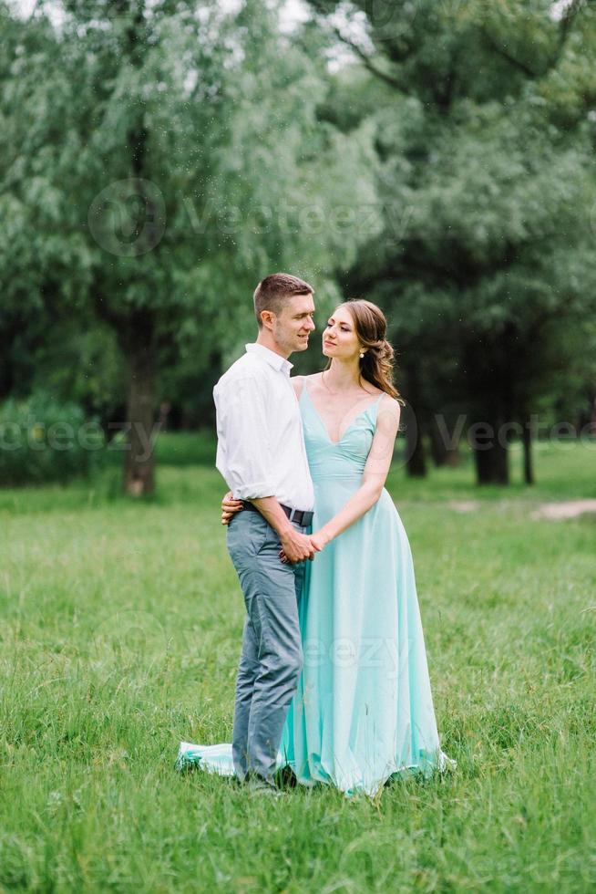 happy guy in a white shirt and a girl in a turquoise dress are walking in the forest park photo