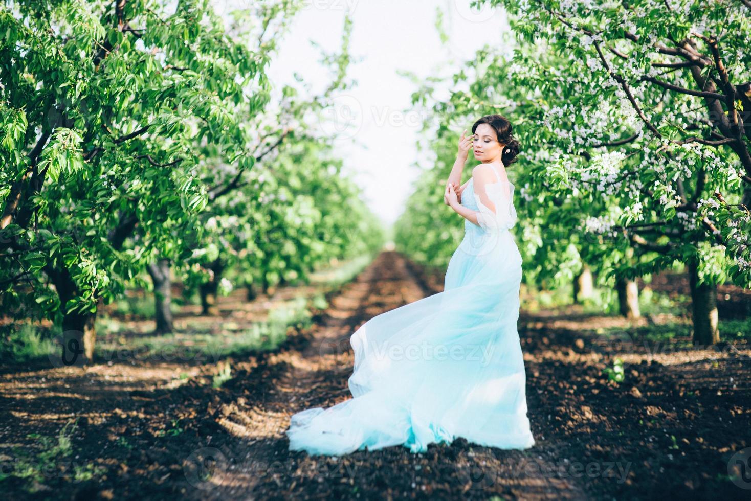 Chica morena con un vestido turquesa en el jardín de primavera foto