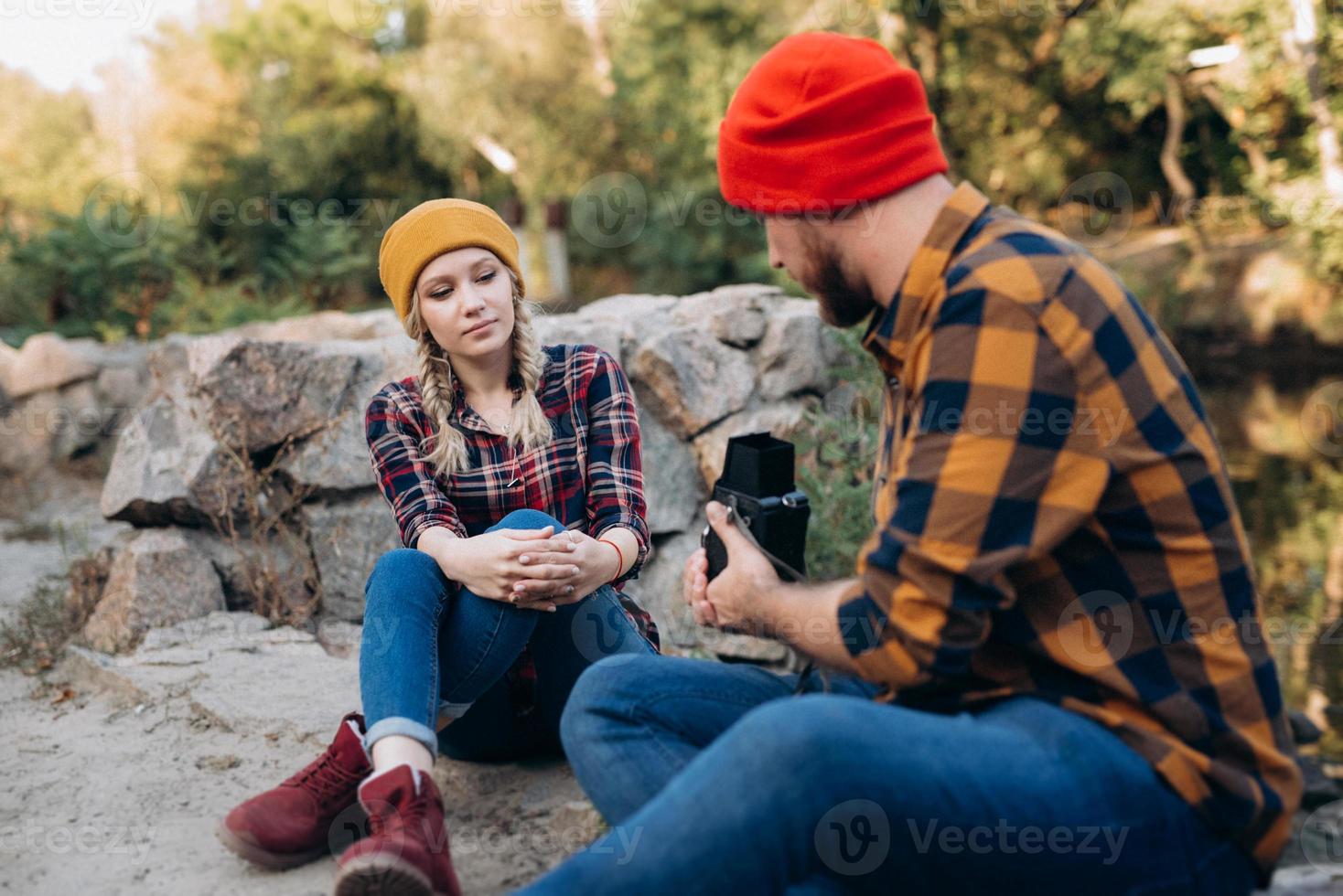 Bald guy with a beard and a blonde girl in bright hats are taking pictures with an old camera photo