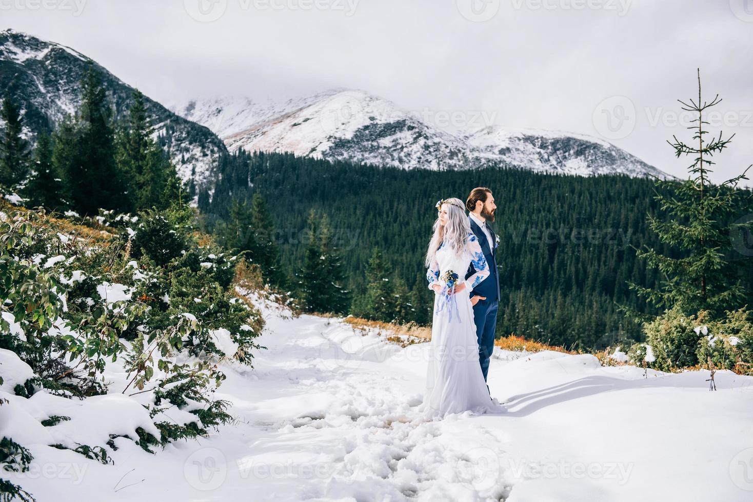 El novio en un traje azul y la novia en blanco en las montañas de los Cárpatos. foto