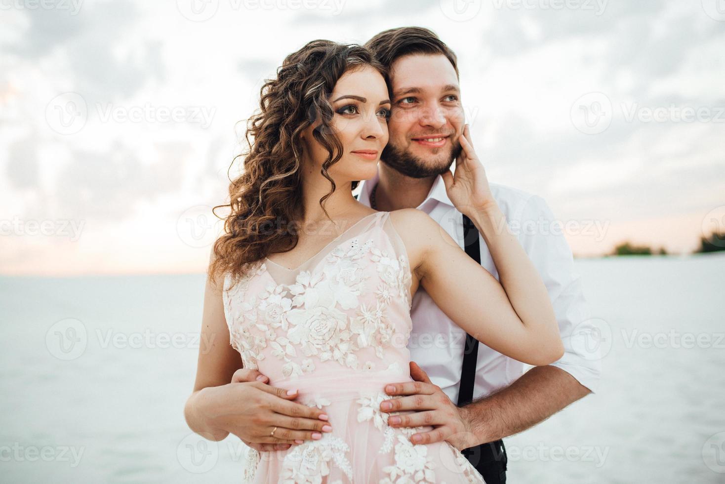 young couple a guy in black breeches and a girl in a pink dress are walking along the white sand photo