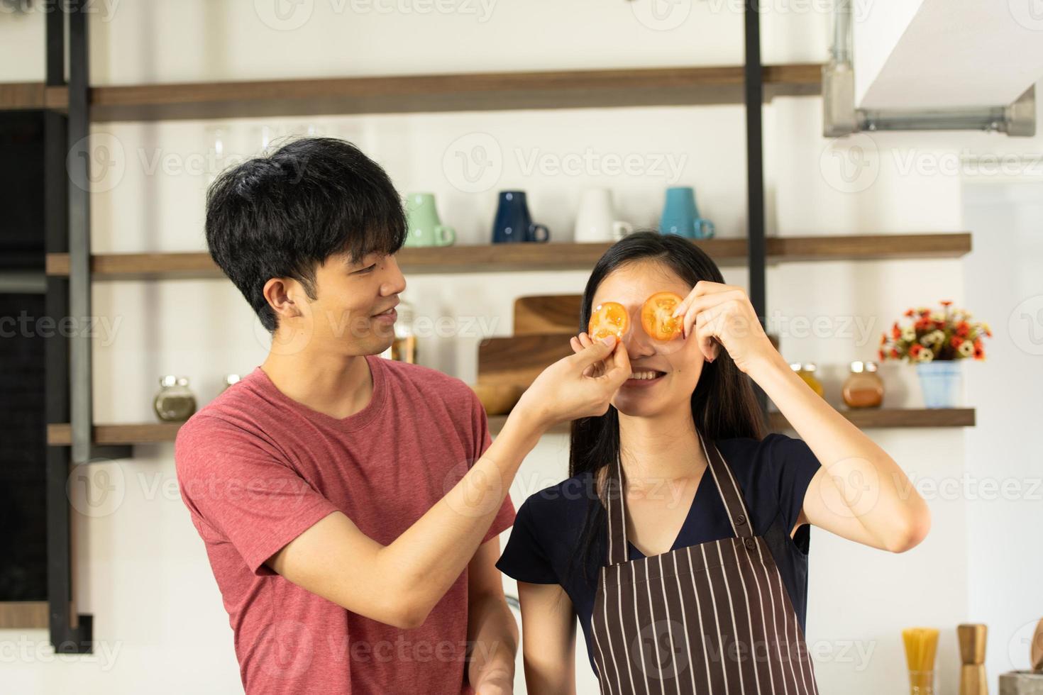 A young Asian couple are eating together and smiling happily while cooking their salad in the kitchen. photo