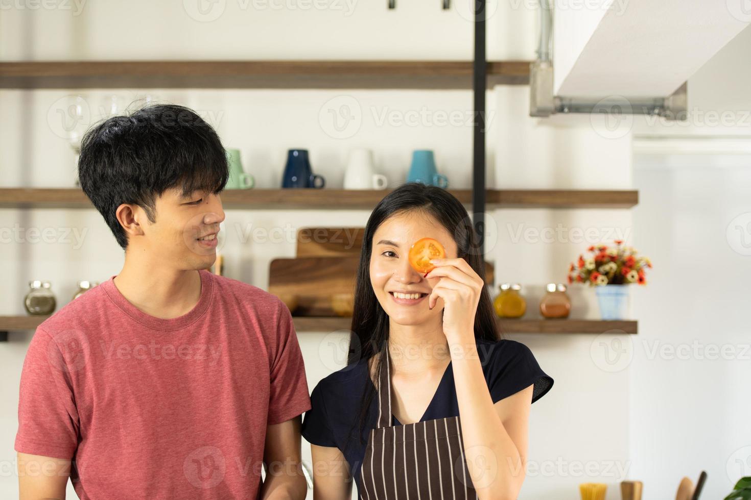 A young Asian couple are eating together and smiling happily while cooking their salad in the kitchen. photo