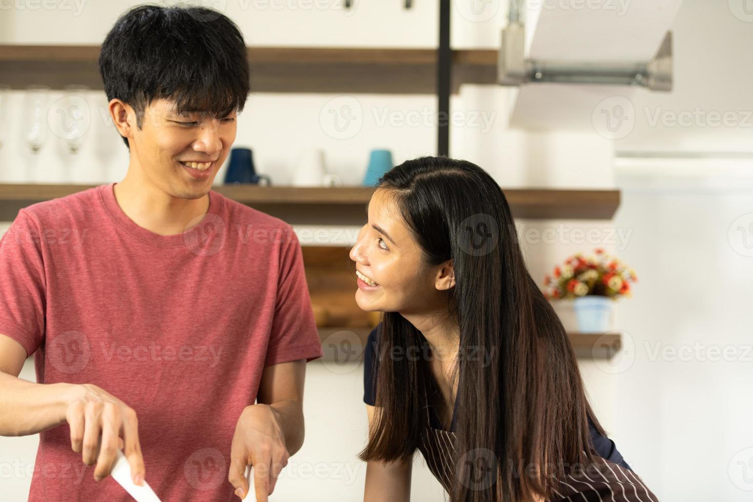 A young Asian couple are eating together and smiling happily while cooking their salad in the kitchen. photo