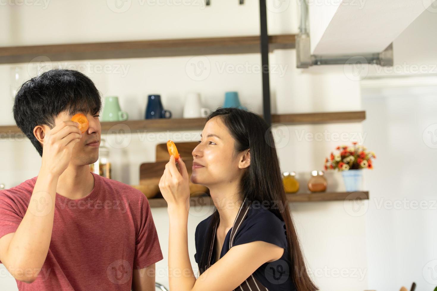 A young Asian couple are eating together and smiling happily while cooking their salad in the kitchen. photo